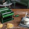 Hands feeding green spinach dough into Marcato Atlasmotor electric pasta machine rollers