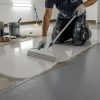 Worker applying epoxy coating to repaired garage floor using roller and squeegee