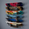 A sleek 5-layer skateboard wall rack mounted on a bedroom wall, holding five colorful decks vertically with graphics on display
