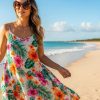 A woman wearing a flowy floral sundress and oversized tortoiseshell sunglasses standing on a sunny beach