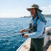An angler wearing a wide brim fishing hat with a neck flap while standing on a sunny boat deck