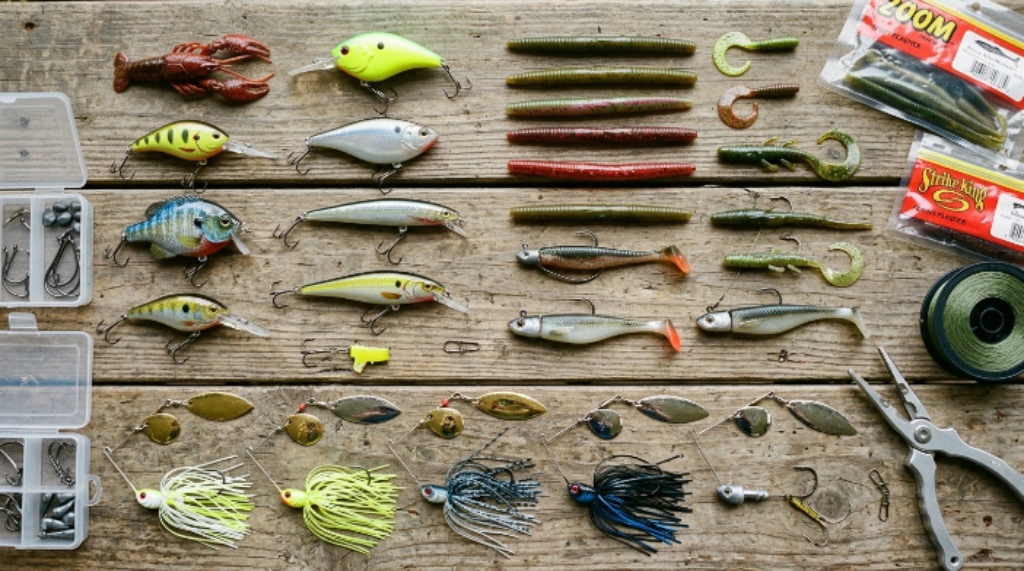 A flat-lay of assorted fishing lures including crankbaits, soft plastics, and spinnerbaits on a wooden surface