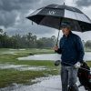 A golfer holding a large UV golf umbrella on a Florida course during a heavy afternoon rainstorm