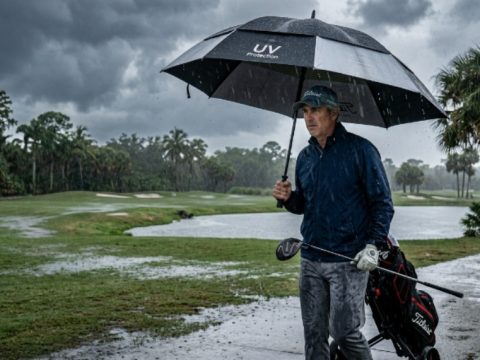 A golfer holding a large UV golf umbrella on a Florida course during a heavy afternoon rainstorm