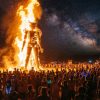 A massive wooden effigy surrounded by towering flames at night during Burning Man 2026 in Nevada's Black Rock Desert, with thousands of participants watching under a star-filled sky