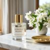 A luxury glass perfume bottle sitting on a marble vanity next to white jasmine flowers.