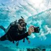 Diver holding a 4K waterproof camera recording turquoise ocean waves.
