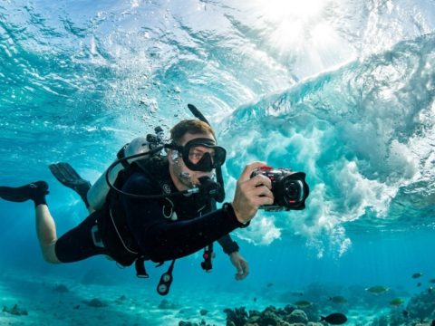 Diver holding a 4K waterproof camera recording turquoise ocean waves.