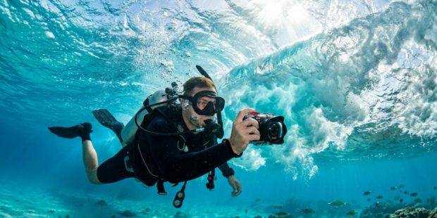 Diver holding a 4K waterproof camera recording turquoise ocean waves.