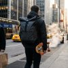 A commuter walking downtown wearing a modern backpack with skateboard straps.