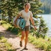 Woman carrying an inflatable paddle board by a lake.